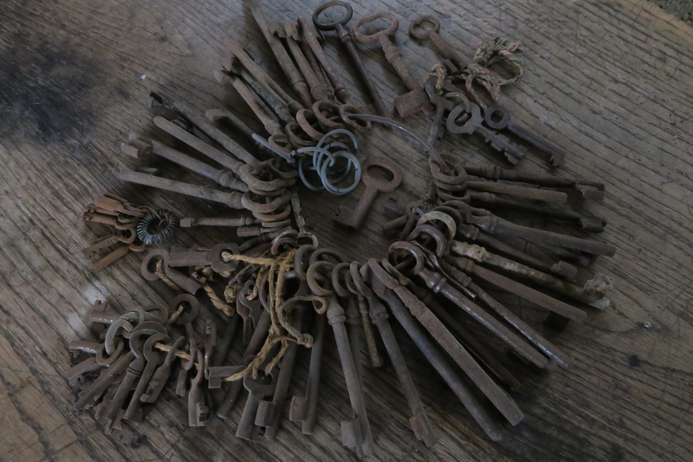 A large bundle of old rusty keys on several rings, spread on a wooden table